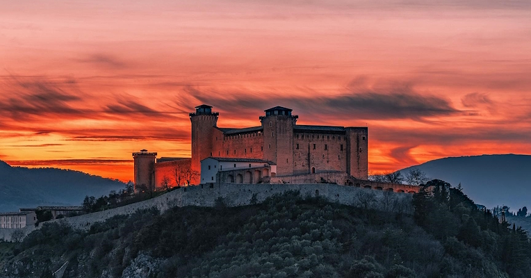 The Albornoz Fortress overlooking the city of Spoleto at sunset, illuminated by a fiery sky