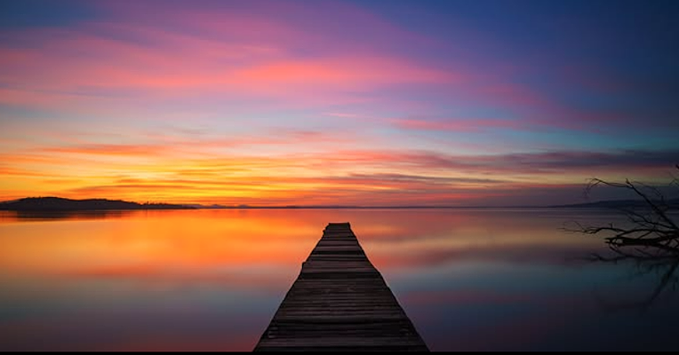 Wooden pier on the waters of Lake Trasimeno, with a sunset sky in shades of blue, purple, and orange reflected on the water.