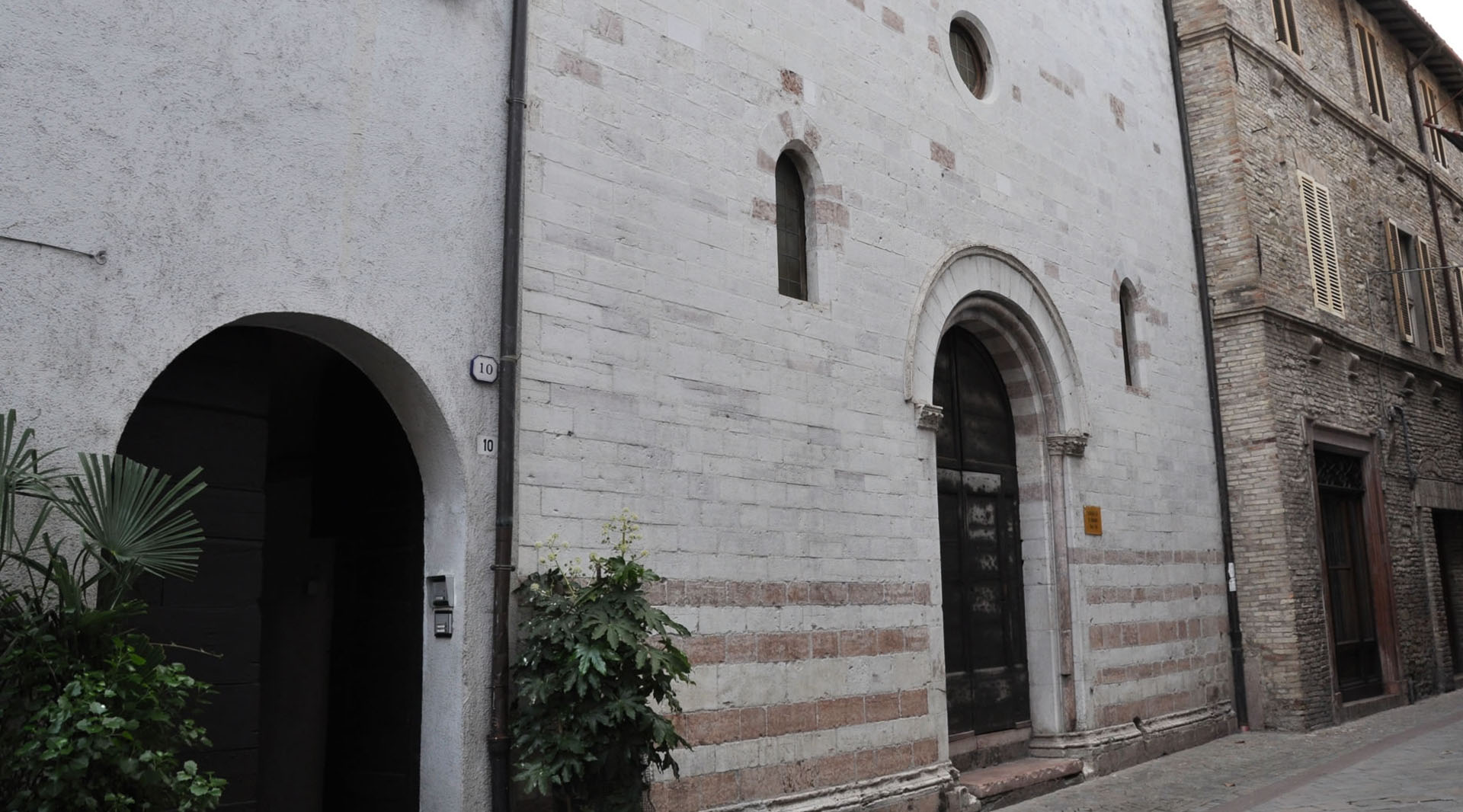 Steinfassade der Kirche San Biagio in Cannara, mit Rundbogenportal und kleinen Fenstern, an einer Straße gelegen.