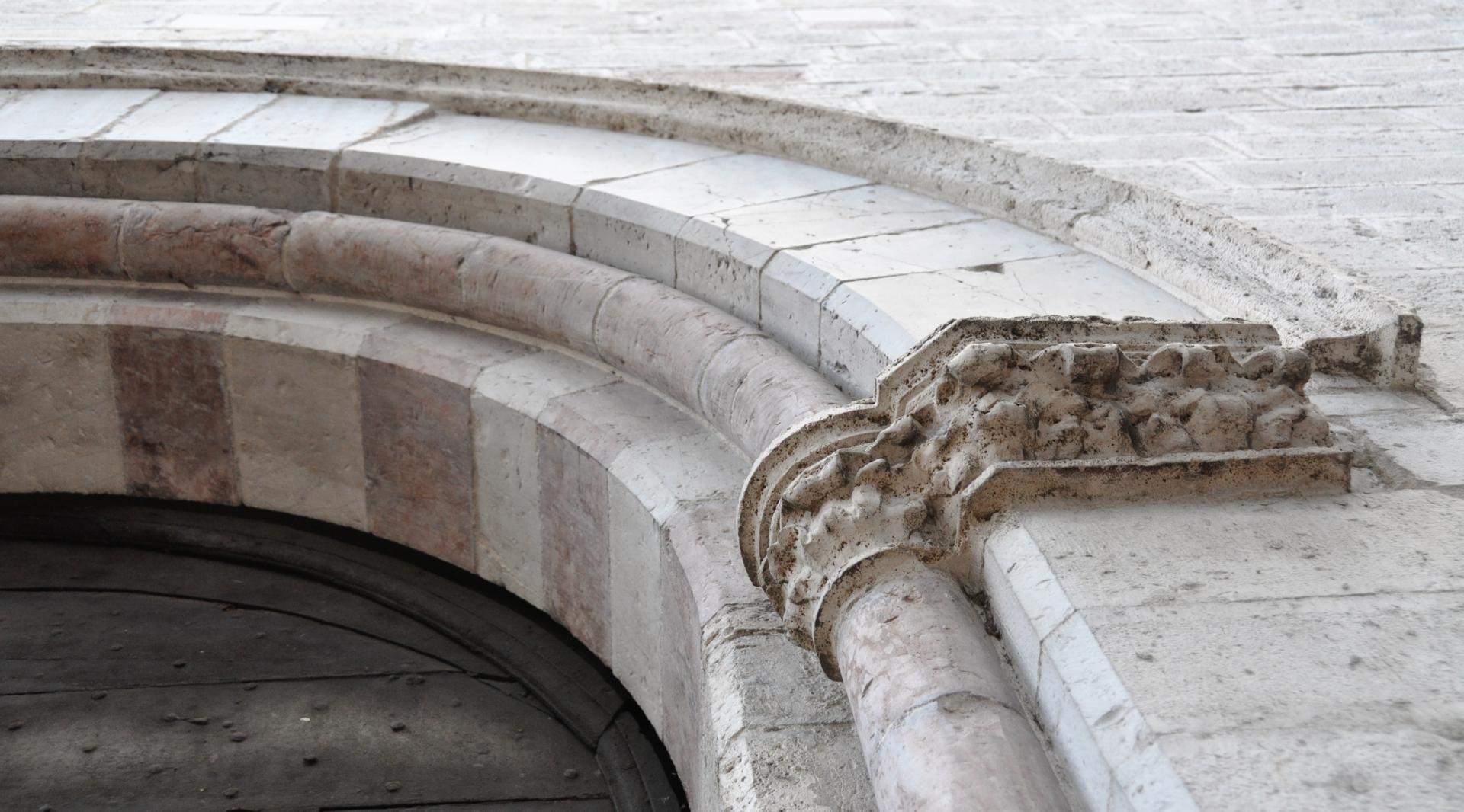Detail des steinernen Rundbogenportals der Kirche, mit einem gemeißelten Kapitell und vom Lauf der Zeit gezeichneten Verzierungen.