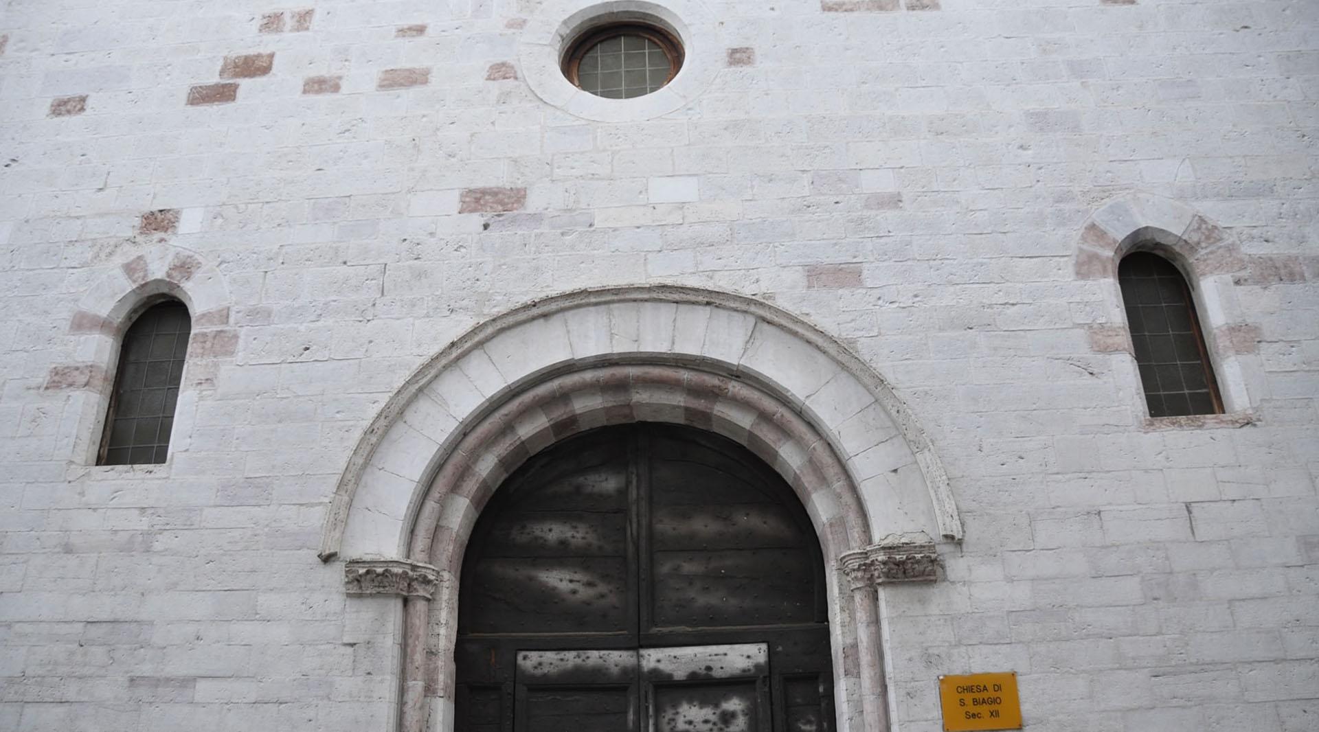 Steinfassade der Kirche San Biagio mit Rundbogenportal, schmalen Fenstern und zentralem Okulus.