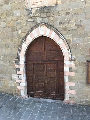 Portale in legno della chiesa di Sant’Agostino a Gualdo Cattaneo, incorniciato da un arco gotico in pietra bicolore.