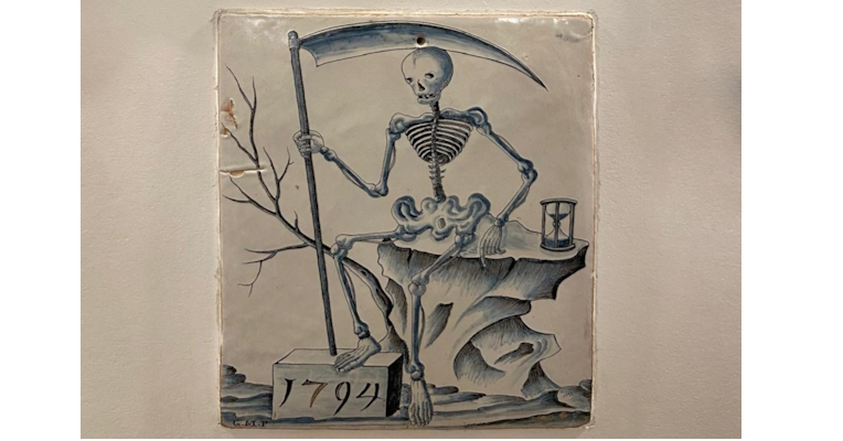 1794 ceramic illustration of a skeleton with a scythe sitting on a rock next to an hourglass.