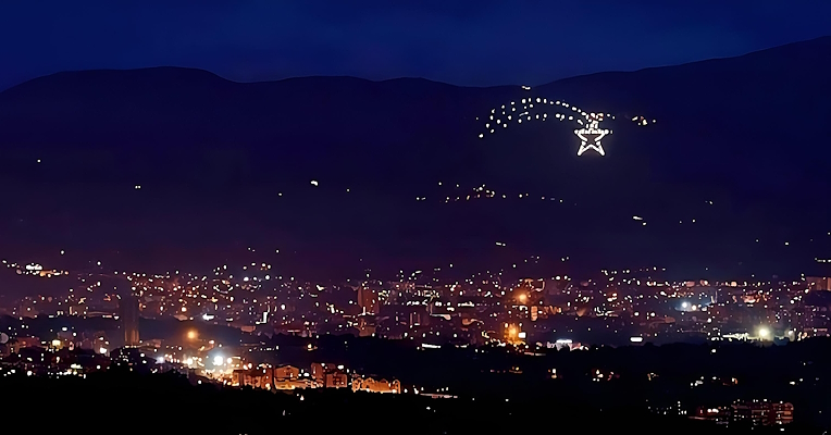 Night view of the illuminated city with the large glowing Christmas star visible on the mountain under a dark blue sky.