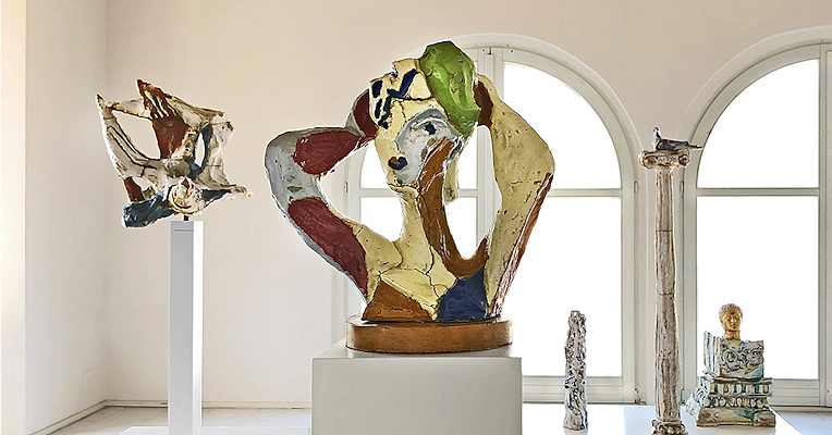 Exhibition room of Palazzo Collicola displaying contemporary ceramic sculptures in vibrant colours, including a central female figure by the artist Leoncillo.