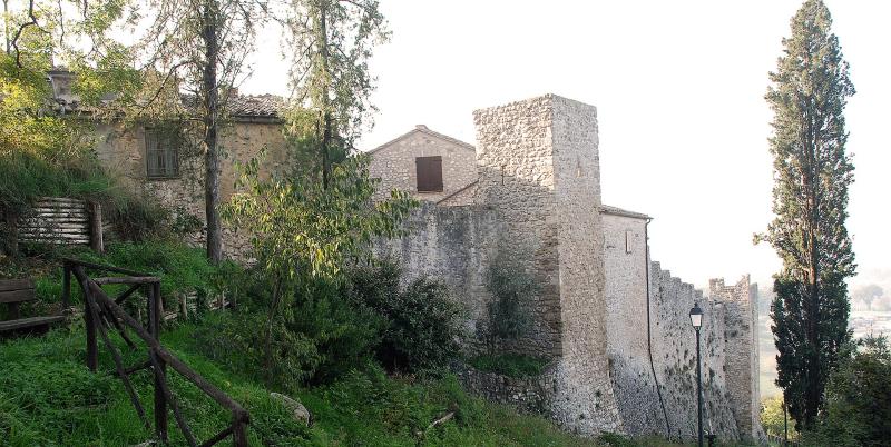 Seitenansicht der Burg von Poggio di Otricoli mit Steinmauern, quadratischem Turm und Vegetation entlang des Hangs.