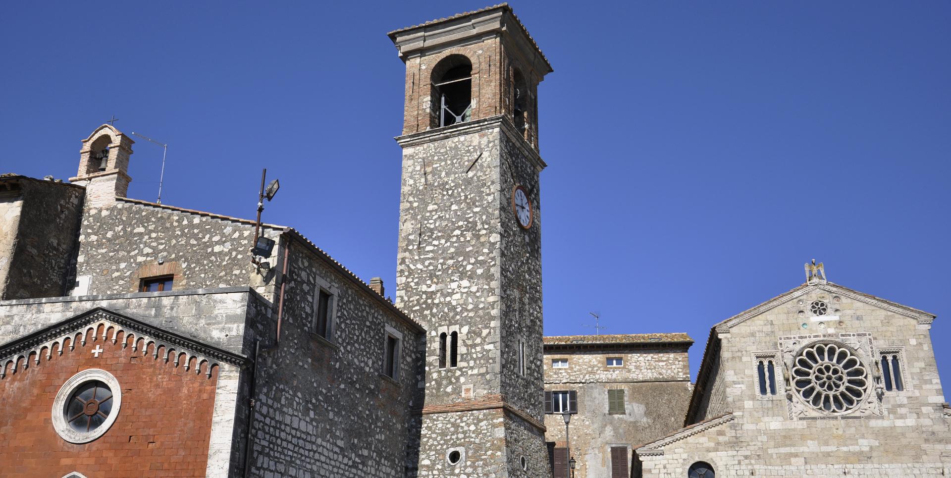 Stone bell tower next to the façade with central rose window of the Church of Santa Maria Assunta