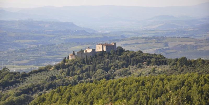 Panoramic view of Castello del Poggio nestled in the greenery of the Umbrian hills, with rolling countryside in the background.