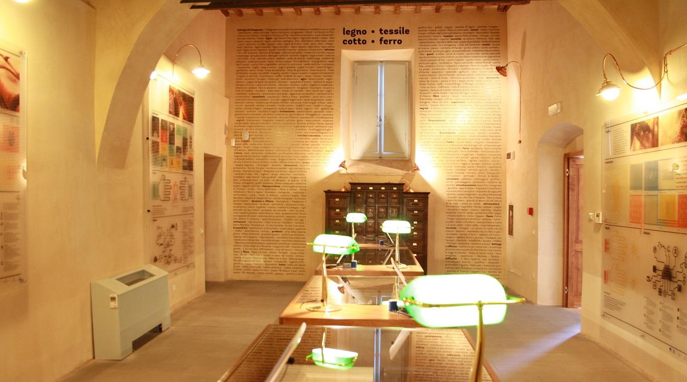 Interior of the "TrasiMemo" room, dedicated to the Memory Bank of Trasimeno. The room is equipped with various display panels along the walls and central desks, each with reading lamps for further exploration.