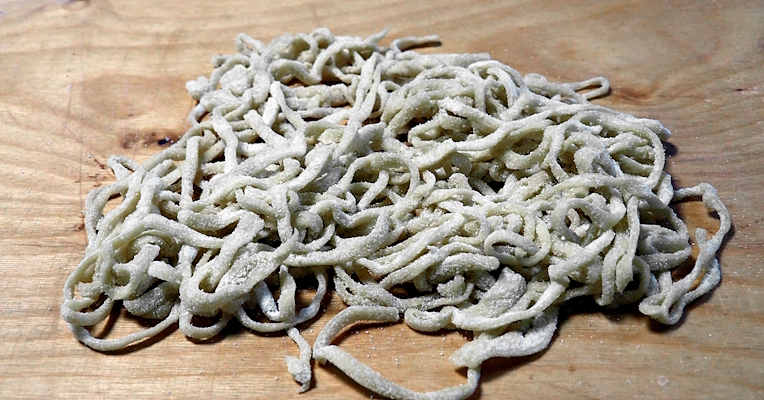 Pile of handmade strangozzi pasta on a wooden board, ready to be cooked.