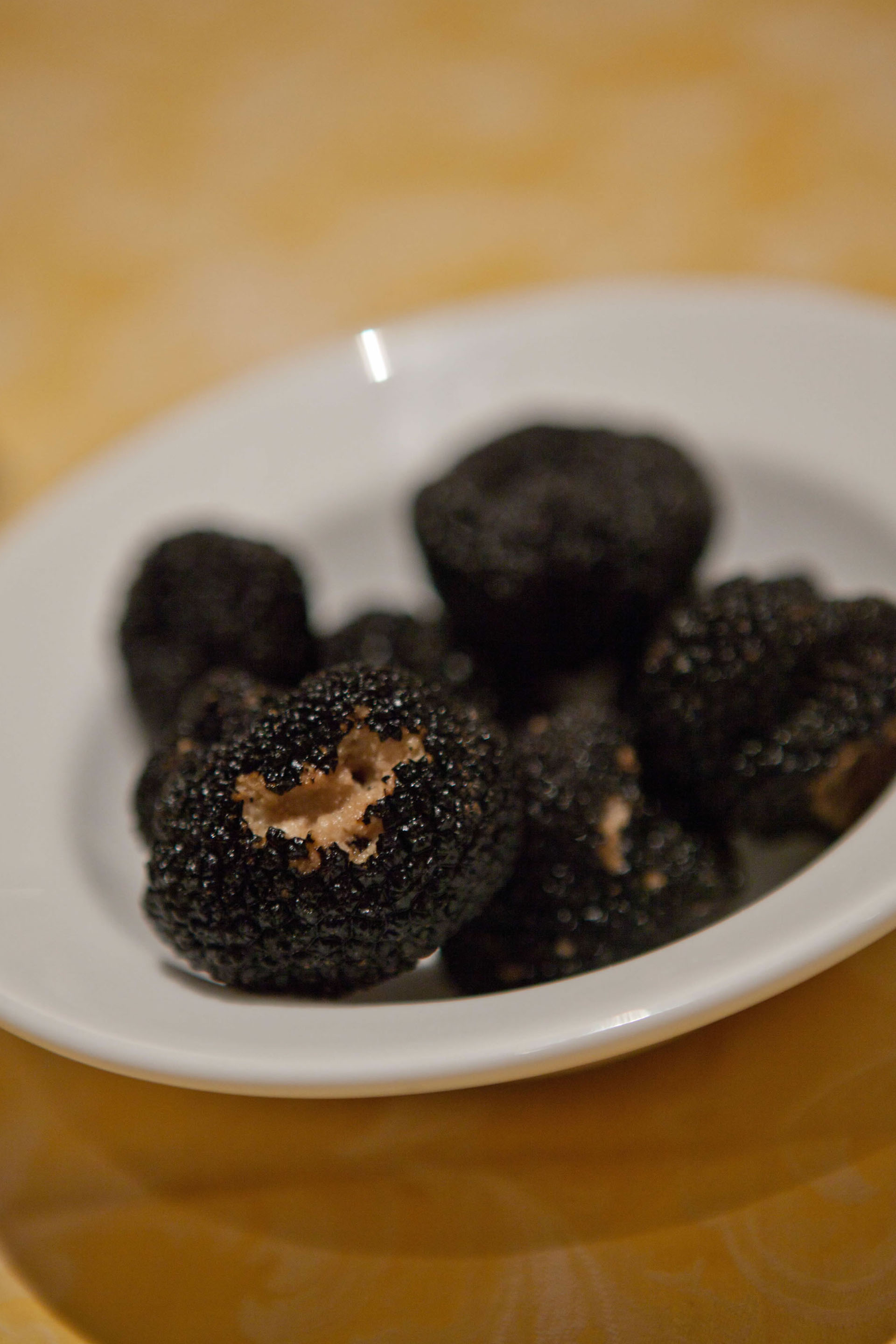 Black truffle on a white plate, with a grainy surface and open sections revealing a light interior.