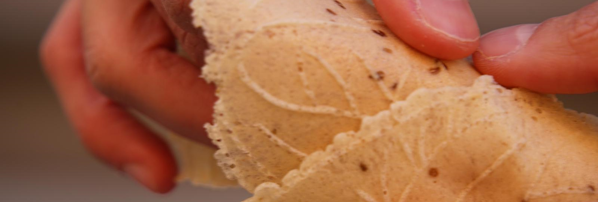 Hände, die eine Tüte aus einer handwerklich hergestellten Waffel mit eingeprägten Mustern und Anissamen halten.