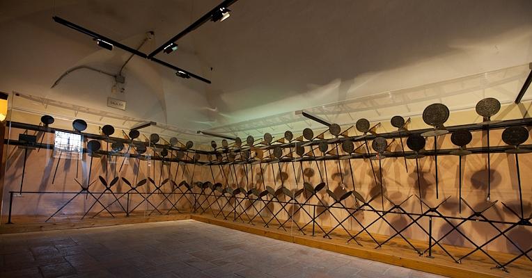 Museumsraum mit einer langen Reihe von eisernen Waffeleisen an den Wänden, sanft beleuchtet.