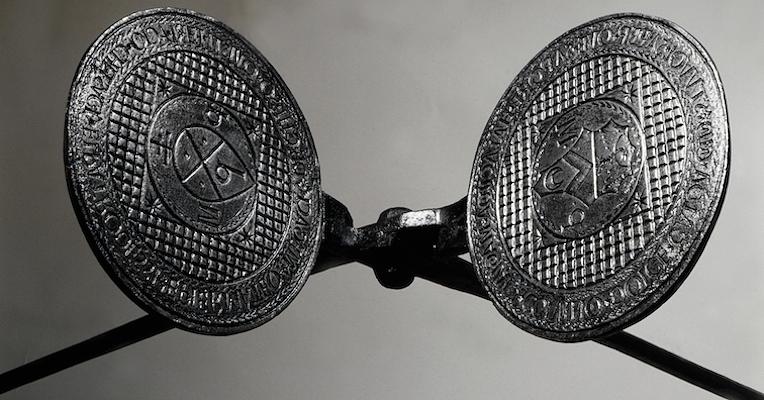 Nahaufnahme eines Waffeleisens mit gravierten Platten und Wappen vor neutralem Hintergrund.