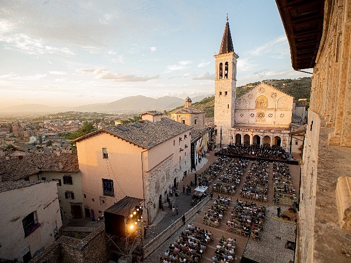 Blick von oben auf die Piazza Duomo in Spoleto während des Festival dei Due Mondi, mit einem sitzenden Publikum vor der Bühne, die vor dem Dom aufgebaut ist.