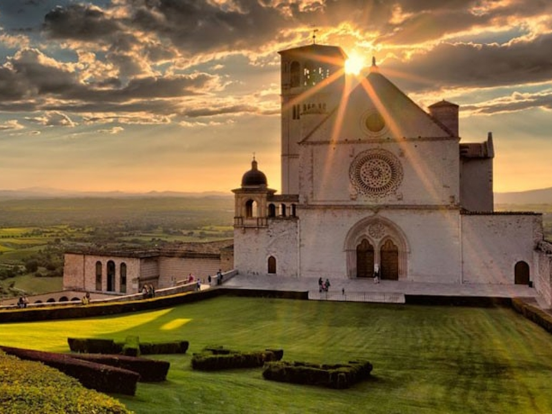 Blick auf die Basilika des Heiligen Franziskus in Assisi, beleuchtet vom Licht des Sonnenuntergangs.