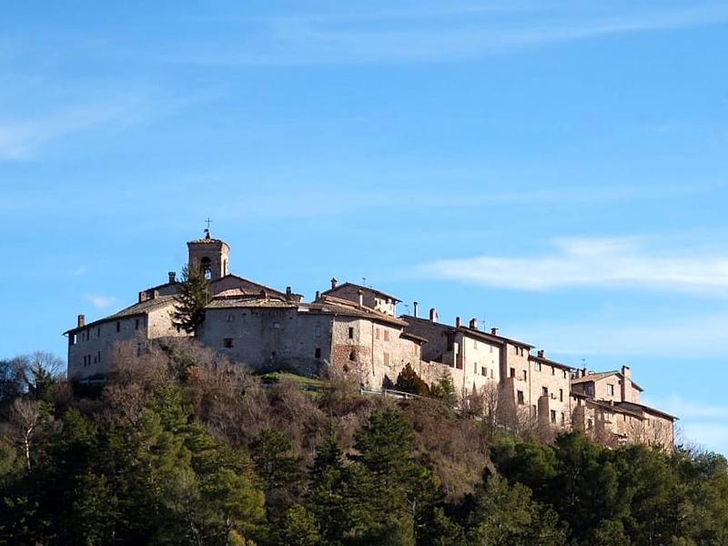 Blick von unten auf die mittelalterliche Burg von Macerino, die auf einem Hügel inmitten der Wälder der Monti Martani thront, mit klarem Himmel im Hintergrund