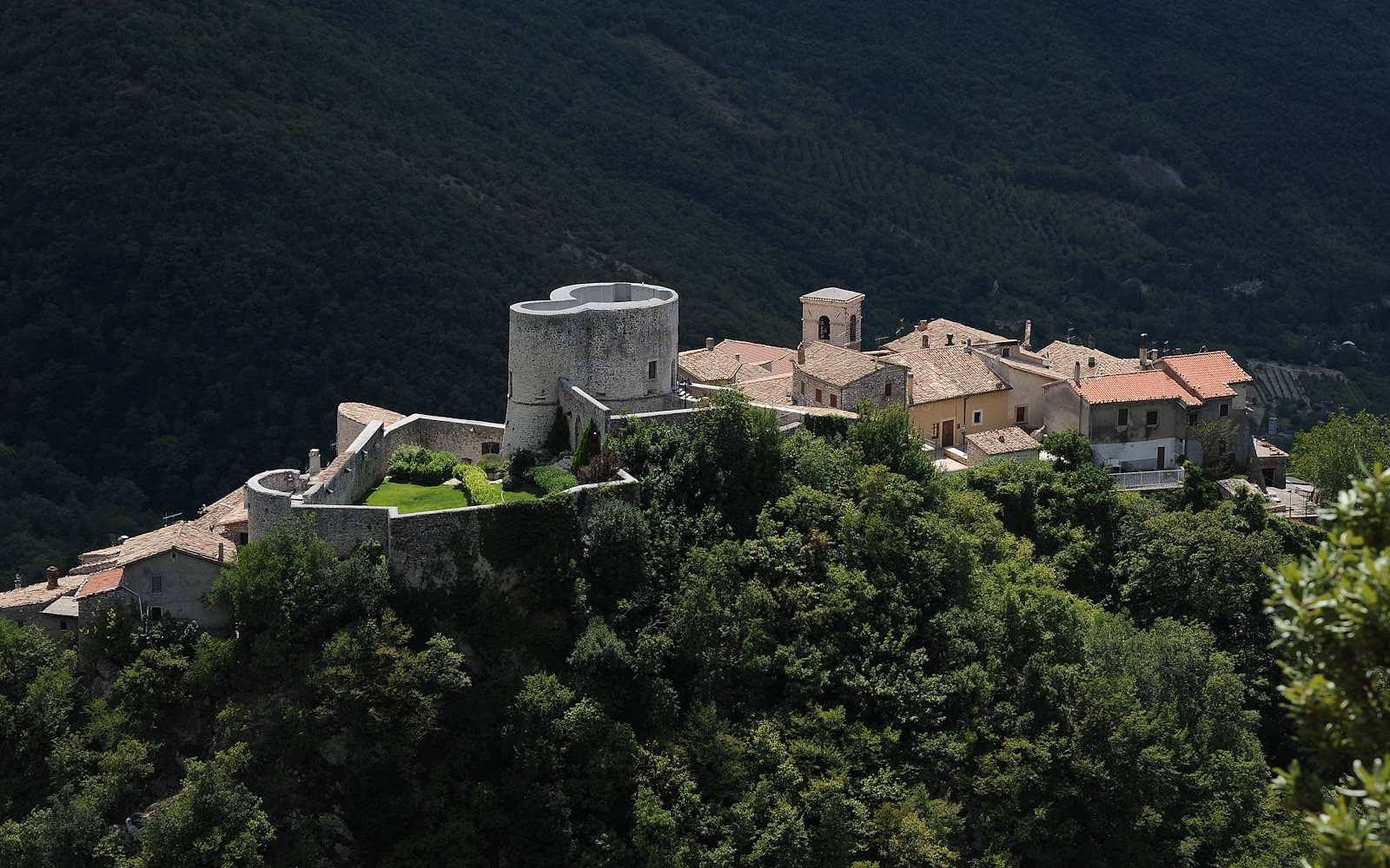 Aerial view of Polino, a medieval Umbrian village with a circular tower and fortified walls, surrounded by green forests.