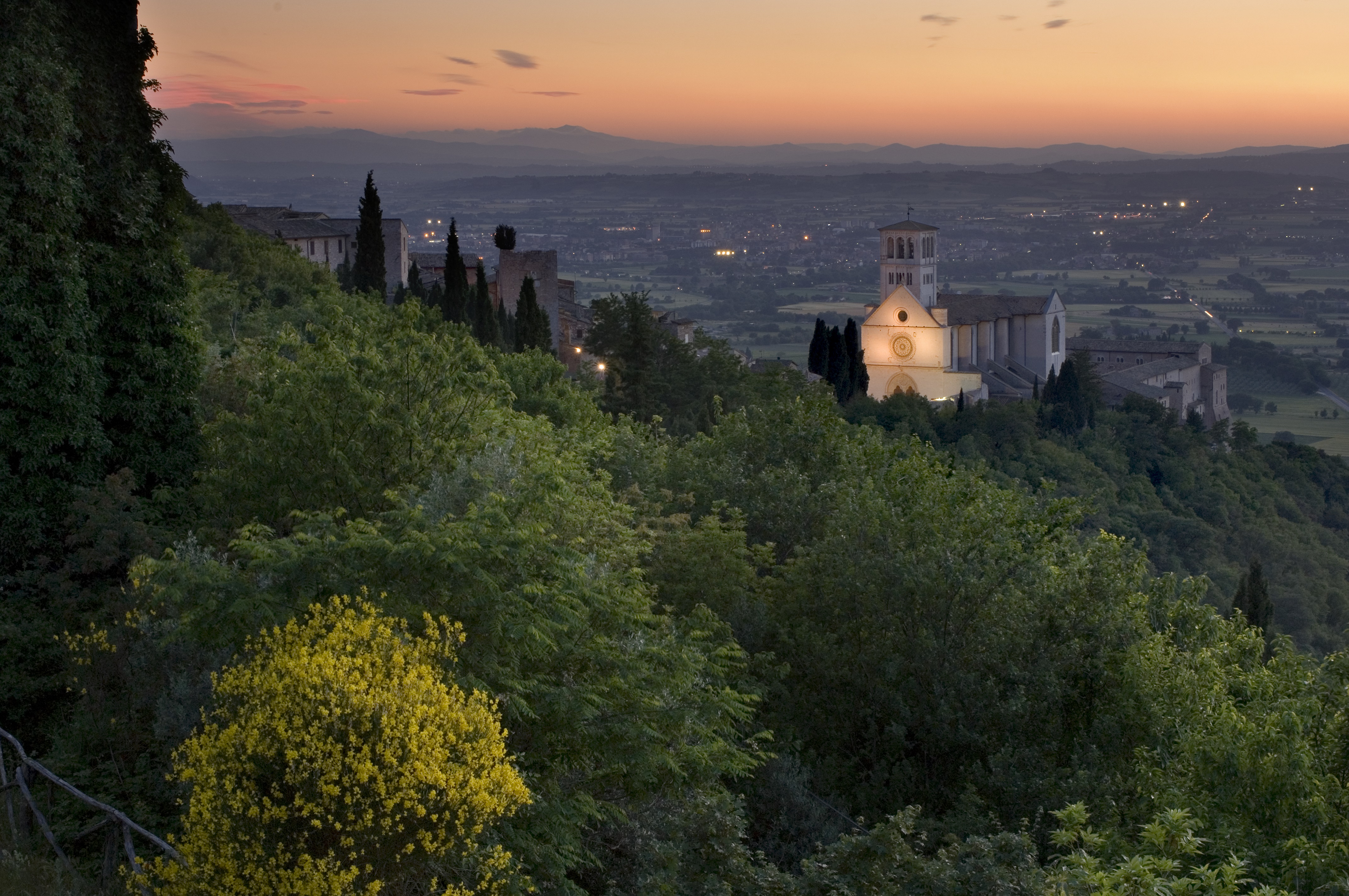 Sonnenuntergang über der Stadt Assisi mit einem herrlichen Blick auf die beleuchtete Basilika des Heiligen Franziskus, die die Landschaft dominiert.