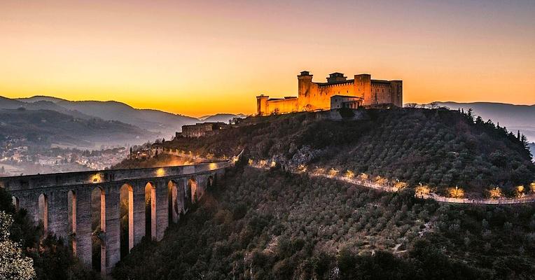 Panoramic view of the Ponte delle Torri and the Rocca Albornoziana illuminated at sunset above the valley and hills around Spoleto.