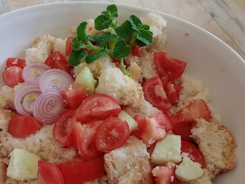 White bowl with panzanella seasoned with cherry tomatoes, cucumbers and sliced onion, garnished with fresh mint