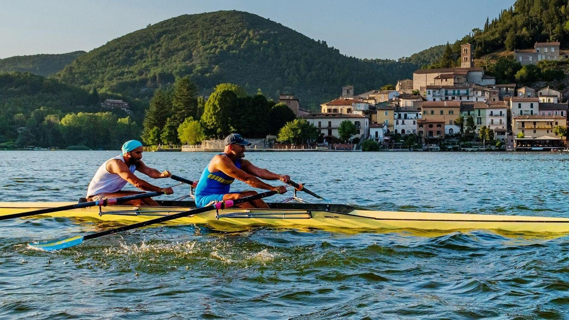 Two rowers on Lake Piediluco, with the lakeside village and green hills in the background